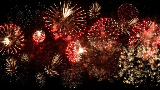 Une vue nocturne d'un ciel illuminé par des feux d'artifice aux couleurs rouges et dorées, éclatant dans des motifs variés.