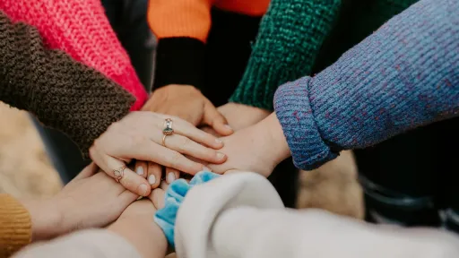 Vue rapproch&eacute;e d'un groupe de personnes portant des pulls aux couleurs vives, superposant leurs mains les unes sur les autres en signe d'unit&eacute; et de soutien mutuel.