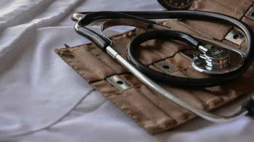Gros plan d'un st&eacute;thoscope noir et d'un tensiom&egrave;tre manuel beige pos&eacute;s sur une blouse m&eacute;dicale blanche.