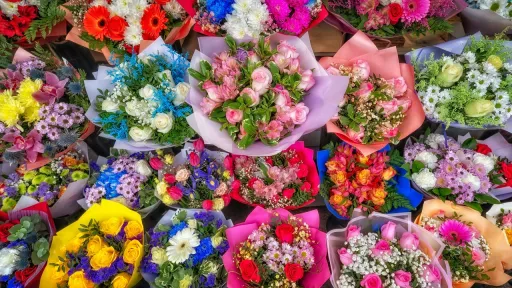 Vue plongeante d'un &eacute;talage serr&eacute; de nombreux bouquets de fleurs vari&eacute;s. On distingue des roses roses, des gerberas rouges et orange, ainsi que des fleurs bleues, jaunes et blanches, le tout envelopp&eacute; dans des papiers cadeaux color&eacute;s.