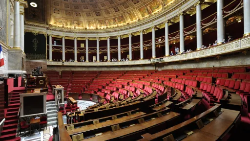 Vue int&eacute;rieure de l'h&eacute;micycle de l'Assembl&eacute;e nationale fran&ccedil;aise, montrant les rang&eacute;es de si&egrave;ges en velours rouge en demi-cercle et l'architecture &agrave; colonnades.