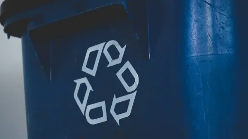 Gros plan sur la paroi d'un bac de recyclage bleu fonc&eacute;, mettant en &eacute;vidence un symbole de recyclage blanc compos&eacute; de trois fl&egrave;ches stylis&eacute;es formant un cercle.