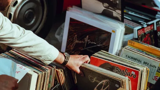 Gros plan sur la main d'une personne en train de parcourir des bacs de disques vinyles vintage lors d'un march&eacute; en plein air. On aper&ccedil;oit plusieurs pochettes d'albums color&eacute;es.